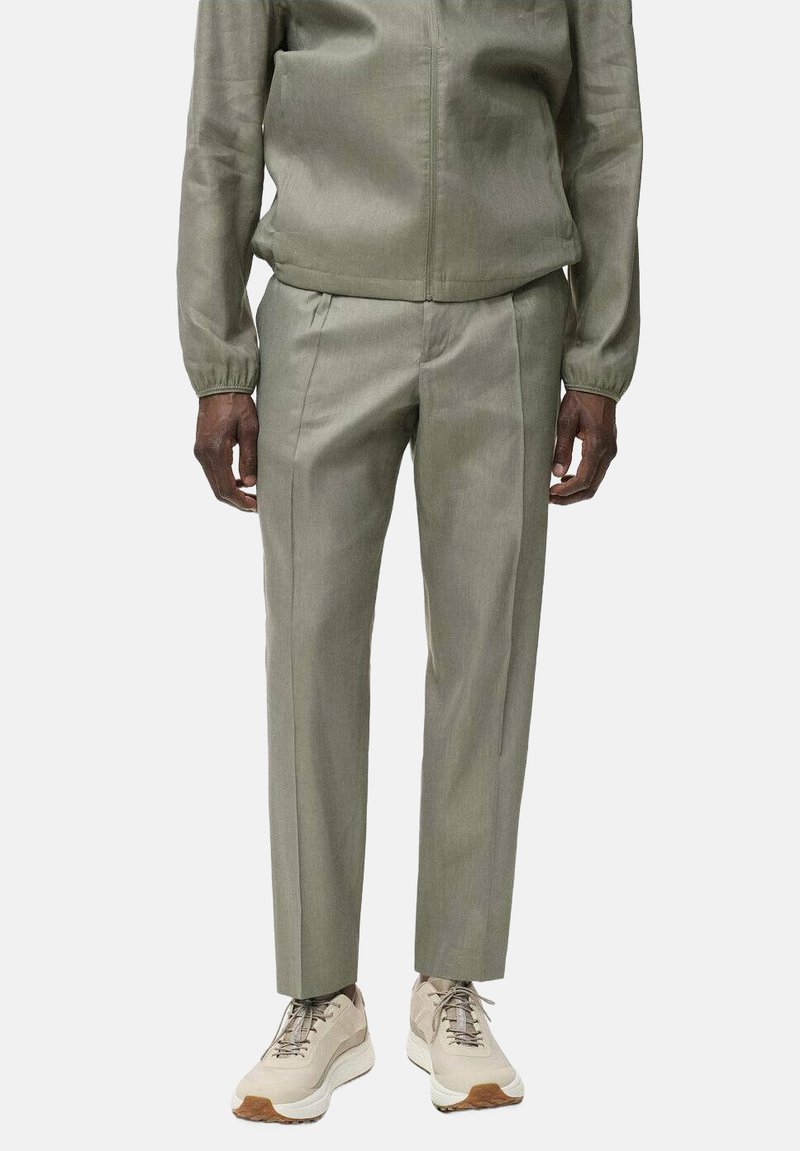 Olivgrüne Trainingsjacke mit elastischen Bündchen, kombiniert mit passenden tapered Hosen. Abgerundet mit beigen Sneakers mit strukturierten Sohlen.