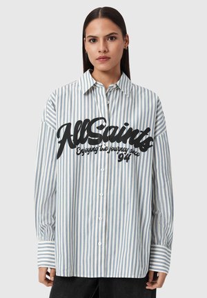 Koszula w paski z guzikami w kolorze białym i niebieskim z dużym czarnym logo tekstowym. Posiada standardowy kołnierzyk oraz długie rękawy z mankietami na guziki.