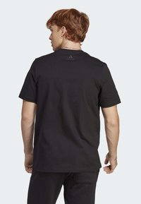 Černé tričko s krátkým rukávem vyrobené z bavlny, s kulatým výstřihem a jemným černým logem adidas na horní části zad.