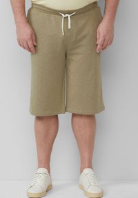 Khakishorts aus weichem Stoff mit einem elastischen Bund und weißem Kordelzug. Verfügt über seitliche Taschen und eine lockere Passform. Getragen mit weißen Sneakern.