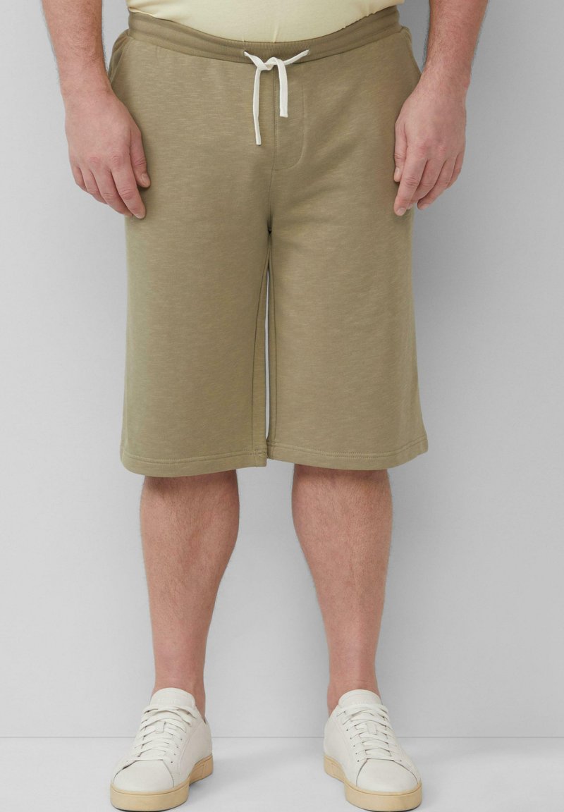 Khakishorts aus weichem Stoff mit einem elastischen Bund und weißem Kordelzug. Verfügt über seitliche Taschen und eine lockere Passform. Getragen mit weißen Sneakern.