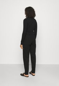 Černý dlouhý rukáv top, kombinovaný s černými kalhotami s vysokým pasem a volánkovým pasem a bočními kapsami, doplněný černými slip-on botami.