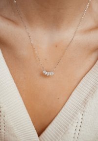 Collana in argento con cinque pietre a forma di goccia, che esaltano un design delicato e curvo. Sfondo con texture e un maglione morbido.