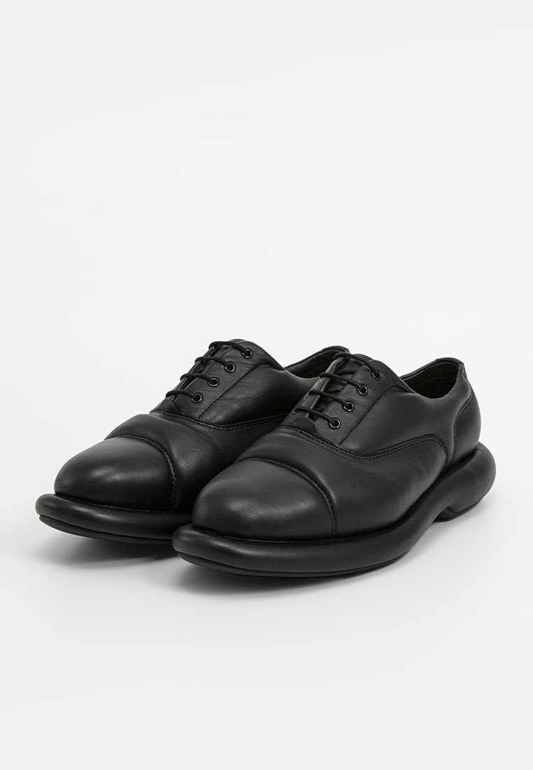 Chaussures en cuir noir avec un bout arrondi, texture lisse, design à lacets et semelle rembourrée. Présente des détails cousus sur la tige.