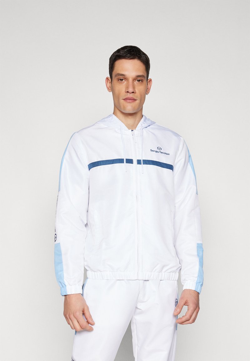 Chaqueta blanca con cremallera y acentos en azul claro, con capucha. Presenta una franja horizontal azul en el pecho y puños elásticos.