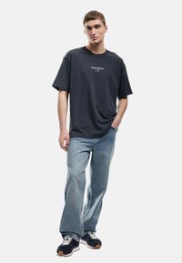 Sort bomulds T-shirt med teksten "HEARTBREAK" i hvid, parret med lyseblå denim jeans og mørke sneakers med hvide accenter.