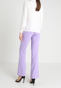 Vit blus med lång ärm och knappdetaljer, ihop med lila utsvängda byxor och svarta högklackade sandaler. Slätt, lättviktsmaterial.