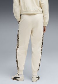 Krämfärgade sweatpants med leopardmönstrade sidopaneler, avsmalnande vid anklarna. Mjuk tyg med elastiskt midjeband; ihopparade med vita sneakers.