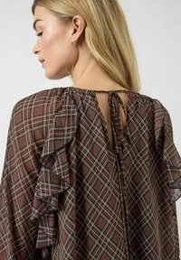Brun rutete topp med volangerm, åpen rygg med knytebånd og lett stoffstruktur.