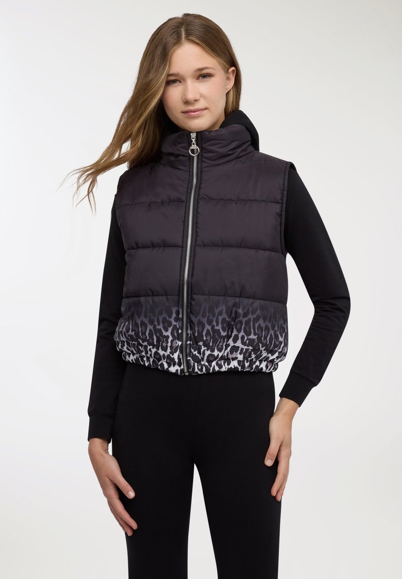 Smanicato imbottito nero con collo alto e chiusura a zip, caratterizzato da un motivo maculato all'orlo. La modella indossa una maglia nera a maniche lunghe.