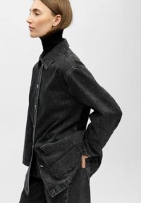 Zwarte denimjack met een kraagontwerp, voorzakken en knoopsluiting. Heeft een ontspannen pasvorm en lange mouwen.