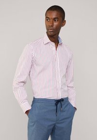 Chemise à rayures blanche avec des lignes verticales rouges, col boutonné et manches longues. Associée à un pantalon bleu clair avec cordon de serrage.