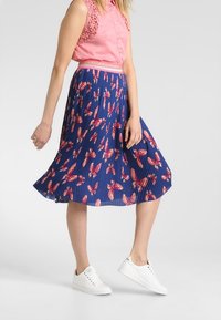 Fållad blå kjol med rosa fjärilstryck, i kombination med en rosa ärmlös skjorta och vita sneakers. Har en figursydd midja.