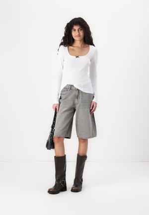 Biała prążkowana bluzka z długim rękawem, szare dżinsowe kuloty, brązowe trapery do kolan oraz czarna torebka na ramię. Prosty, casualowy zestaw.