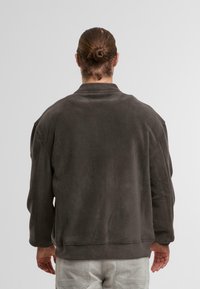 Felpa in poliestere grigio scuro con colletto alto, spalle scese e polsini a coste. Tessuto morbido e cuciture minime per un design pulito.