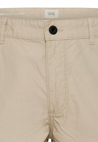 Beige regular fit trousers with black button closure, belt loops, and visible stitching details on waistband and fly area.