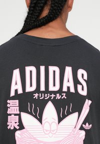Črna grafika majica s kratkimi rokavi z bold roza napisem "ADIDAS" in risbo nasmejanih rezancev s palčkami in logotipom cveta.
