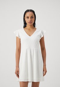 Vit bomullsklänning med V-ringning, volangärmar och broderat mönster. Utsvängd design som slutar ovanför knäet och har en mjuk textur.