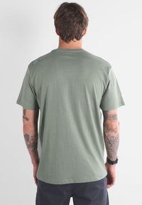 T-shirt en coton vert olive avec col rond et manches courtes, doté d'un petit logo sur l'épaule et d'une texture lisse.