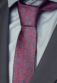 Burgundy silke slips med et paisley-mønster i nuancer af blå og rød, båret over en lysternet skjorte og en grå jakkesætjakke.