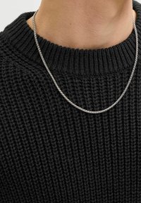 Zbliżenie na srebrny skręcony naszyjnik noszony na szyi osoby, na tle teksturowanego czarnego swetra dzianinowego.