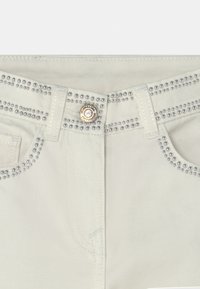 Białe dżinsy z srebrnymi ćwiekami wzdłuż pasa i kieszeni, z zapięciem na złoty guzik i mocnym denimu.