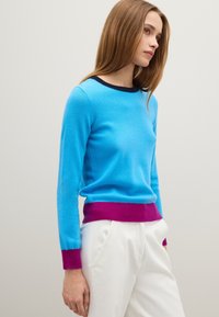 Maglione azzurro chiaro in cashmere con scollo rotondo, bordi blu navy scuri e dettagli fucsia ai polsini e all'orlo. Design aderente.