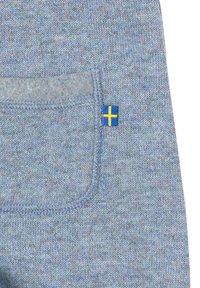 Ljust blått stickat tyg med en liten ficka och en svensk flagga i gult och blått, med en slät textur och subtilt mönster.