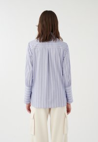 Chemise rayée bleu clair à manches longues avec poignets boutonnés. Dotée d'un empiècement dos et d'une coupe décontractée. Le tissu est lisse avec un léger éclat.