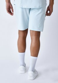 Pantaloni sportivi azzurri chiari con tasca laterale, indossati con calze bianche fino al ginocchio e sneakers bianche, che mostrano una texture di tessuto liscia.