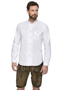 Weißes Langarmhemd mit Stehkragen, versehen mit dekorativen Nähten und goldenen Knöpfen. Kombiniert mit braunen Lederhosen, verziert mit floralen Mustern.