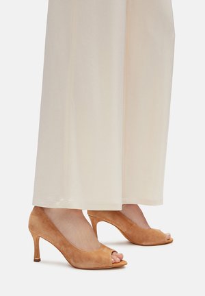 Zapatos de tacón peep-toe de ante en color beige claro con un diseño curvado modesto y una altura de tacón de 5 cm, complementados con un acento dorado en el tacón.