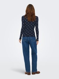 Marineblå langærmet top med hvide polkaprikker, ribbet struktur, kombineret med lyseblå jeans med lige ben og brune ankelstøvler.