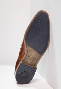 Chaussure habillée en cuir marron avec une semelle en caoutchouc noire texturée, dotée d'un design anti-choc et de détails de marque en relief.