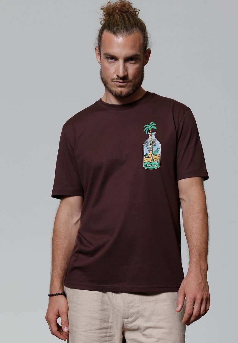 Bordeauxfarbenes Baumwoll-T-Shirt mit kurzen Ärmeln, das auf der linken Brustseite ein Grafikbild eines Palmenbaums in einer Flasche zeigt. Glatte Textur.