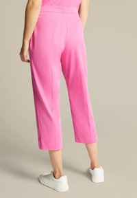 Roze cropped broeken van een gladde, lichte stof met zijsplitten, gecombineerd met witte sportschoenen.