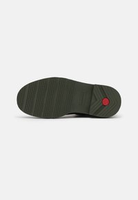 Semelle en caoutchouc verte avec une surface texturée, présentant des motifs de semelle et un accent rouge. Nom de la marque imprimé sur le côté pour identification.