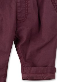 Burgunderfarbene Baumwollhose mit umgeschlagenem Saum, versehen mit einer Seitentasche und sichtbar genähten Nähten. Glatte Textur und taillierte Passform.