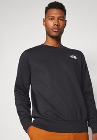 Schwarzer Sweatshirt mit langen Ärmeln und Rippbündchen. Verfügt über ein kleines weißes Logo auf der Brust. Weicher Stoff mit einem klassischen Rundhalsausschnitt.