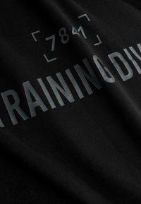 Czarna bawełniana koszulka z dużym szarym napisem "TRAINING DIV" oraz numerami "7841", o miękkiej, gładkiej strukturze.