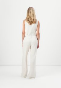 Top senza maniche di un beige chiaro abbinato a pantaloni larghi di colore crema, con una texture liscia e un sottile design sartoriale.