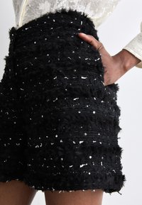 Pantalones cortos negros hechos de una tela texturizada con lentejuelas, con un diseño en capas y un corte holgado. Cintura elástica con bolsillos laterales.