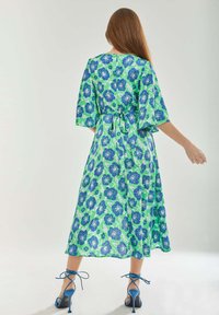 Floral midi dress in green and blue with short, wide sleeves and a tie waist detail, featuring a vibrant floral pattern throughout.