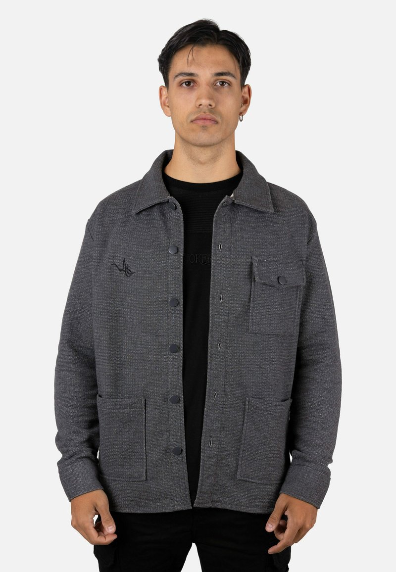 Chaqueta gris con cierre de botones, acabado texturizado, dos bolsillos frontales y diseño de cuello con solapa. Cuenta con botones negros y detalles sutiles.