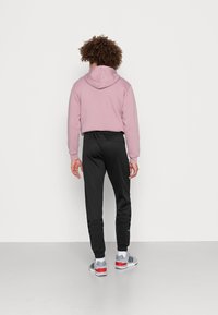 Rosa huvtröja med luva, kombinerad med svarta joggers med randiga detaljer nära fållen. Grå sportskor med röda och blå detaljer.