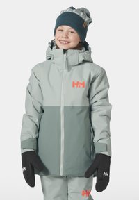 Světle šedá nepromokavá bunda s tmavě šedým spodkem, růžovým logem a nastavitelnou kapucí. V kombinaci s černými palčáky. Pletená čepice s bambulí.