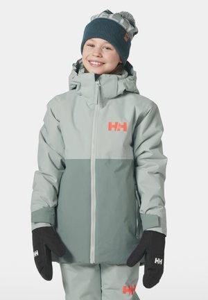 Chaqueta impermeable gris claro con parte inferior gris más oscuro, logo rosa y capucha ajustable. Combinada con manoplas negras. Gorro de punto con pompón.