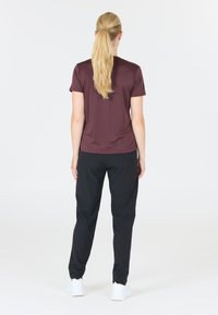 Vinröd kortärmad topp med en mjuk textur, tillsammans med svarta avsmalnande byxor. Vita sneakers fulländar outfiten. Bakifrån visad.