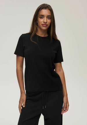 Czarny bawełniany t-shirt z krótkim rękawem, okrągłym dekoltem i luźnym krojem, zestawiony z czarnymi dresami. Gładka tekstura, bez widocznych wzorów.