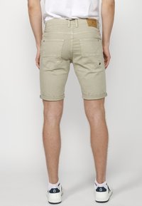 Pantalones cortos de mezclilla beige con puños enrollados, que presentan un diseño texturizado en el bolsillo trasero y una etiqueta de cuero marrón en la cinturilla.
